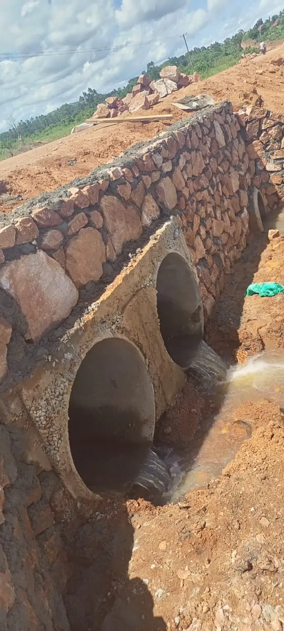 Twin concrete culverts set into a hand-packed stone headwall discharging water below a new road embankment