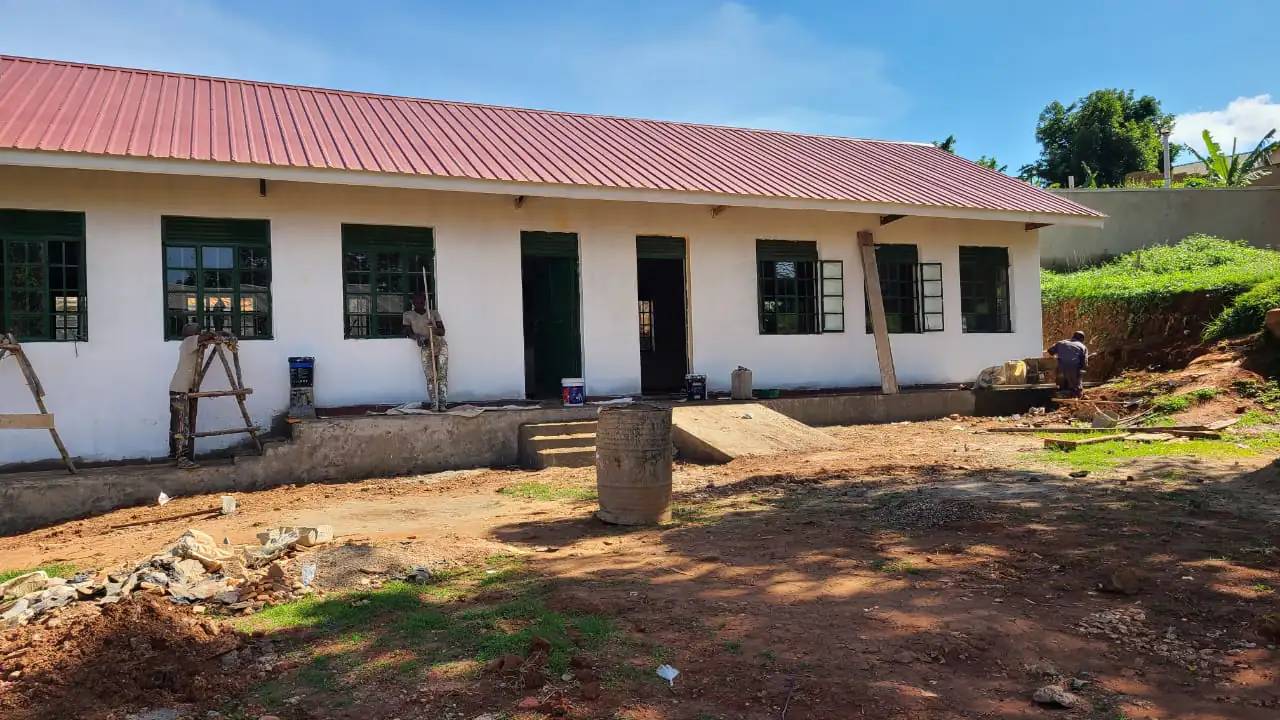 Painters finishing the walls of a completed classroom block with a red sheeted roof and green window frames