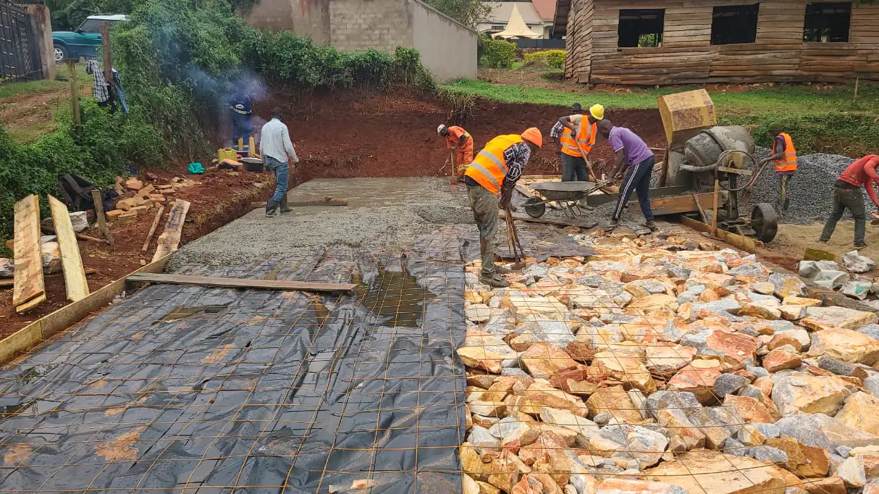 Crew placing and levelling concrete over mesh reinforcement and hardcore, with a site mixer running